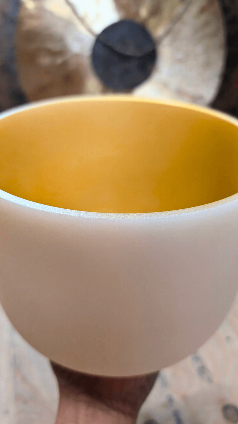 A sound practisioner upholding a gold-colored crystal singing bowl with a gong in the background