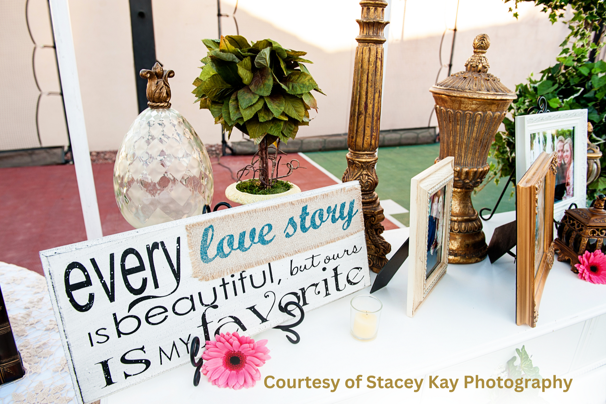 Elegant LDS wedding reception decor featuring gold accents, framed photos, greenery, and a rustic sign reading “Every love story is beautiful, but ours is my favorite,” symbolizing faith-centered celebration and personal wedding style. Image courtesy of Stacey Kay Photography.