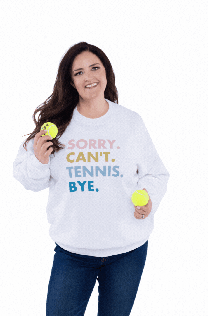 Carrie, smiling holding two tennis balls in a sweatshirt that sayd sorry can't tennis bye