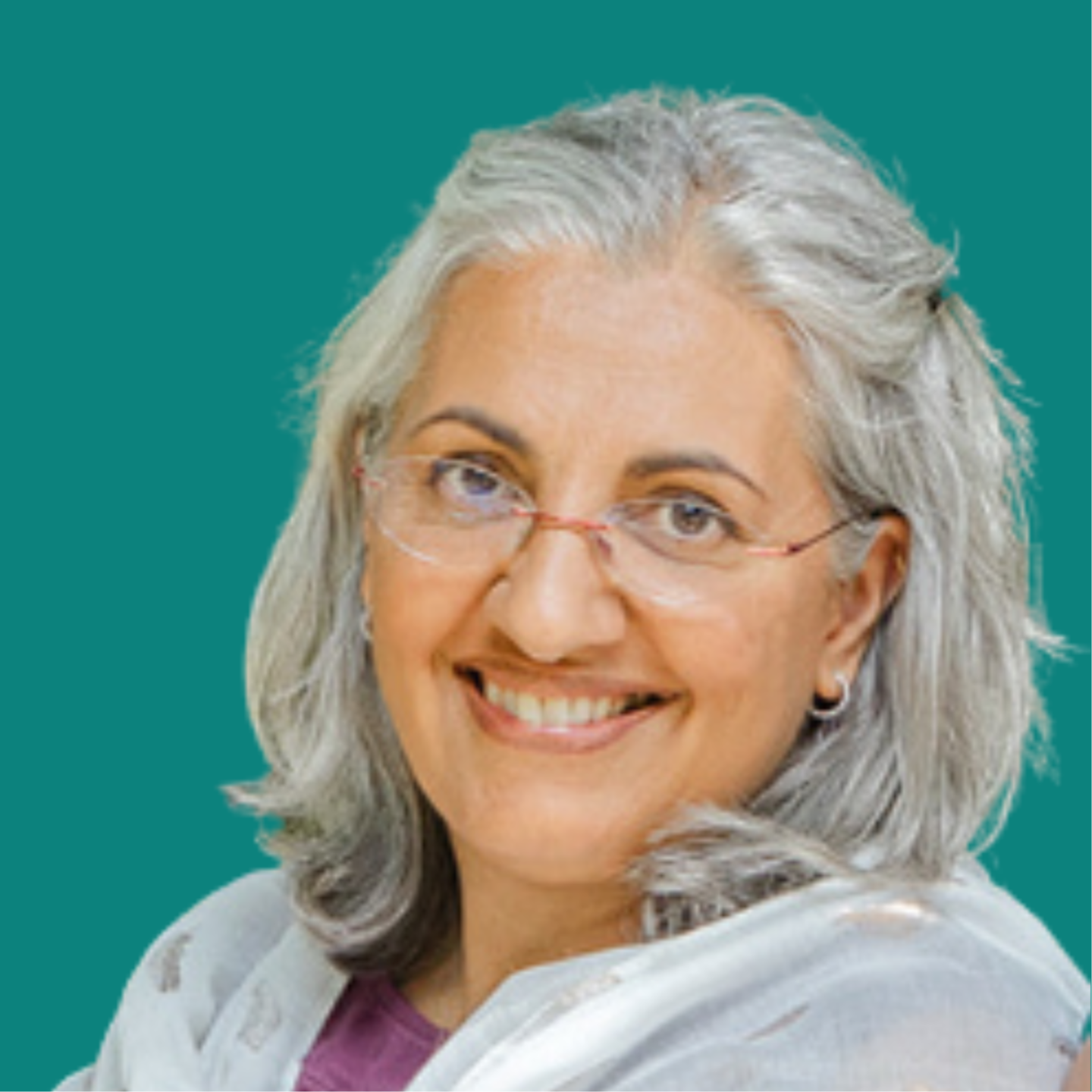 A headshot of Shehnaaz Latif smiling sideways at the camera with short grey hair, a scarf round her neck, a purple top and glasses with brown skin tone