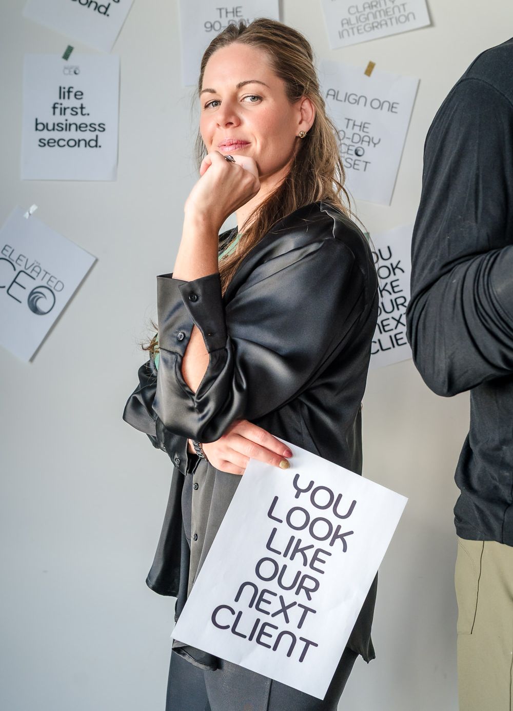 Danielle Grant (Your Mindset Mentor) holding a sign that says 'you look like our next client', with her left hand under her chin, showcasing a power pose and invitation to their new client