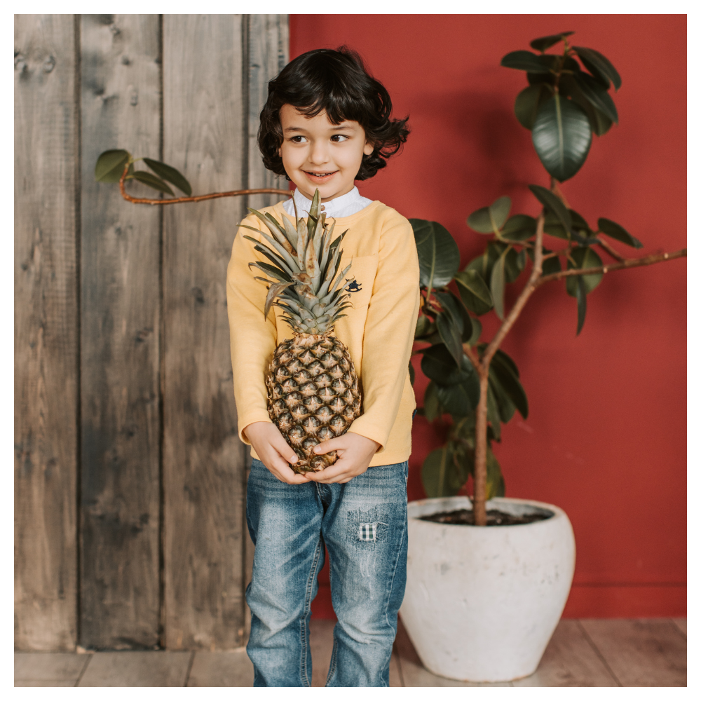 Smiling young child holding a pineapple indoors, representing playful learning, creativity, and intentional childhood moments inspired by Serenely Rooted.