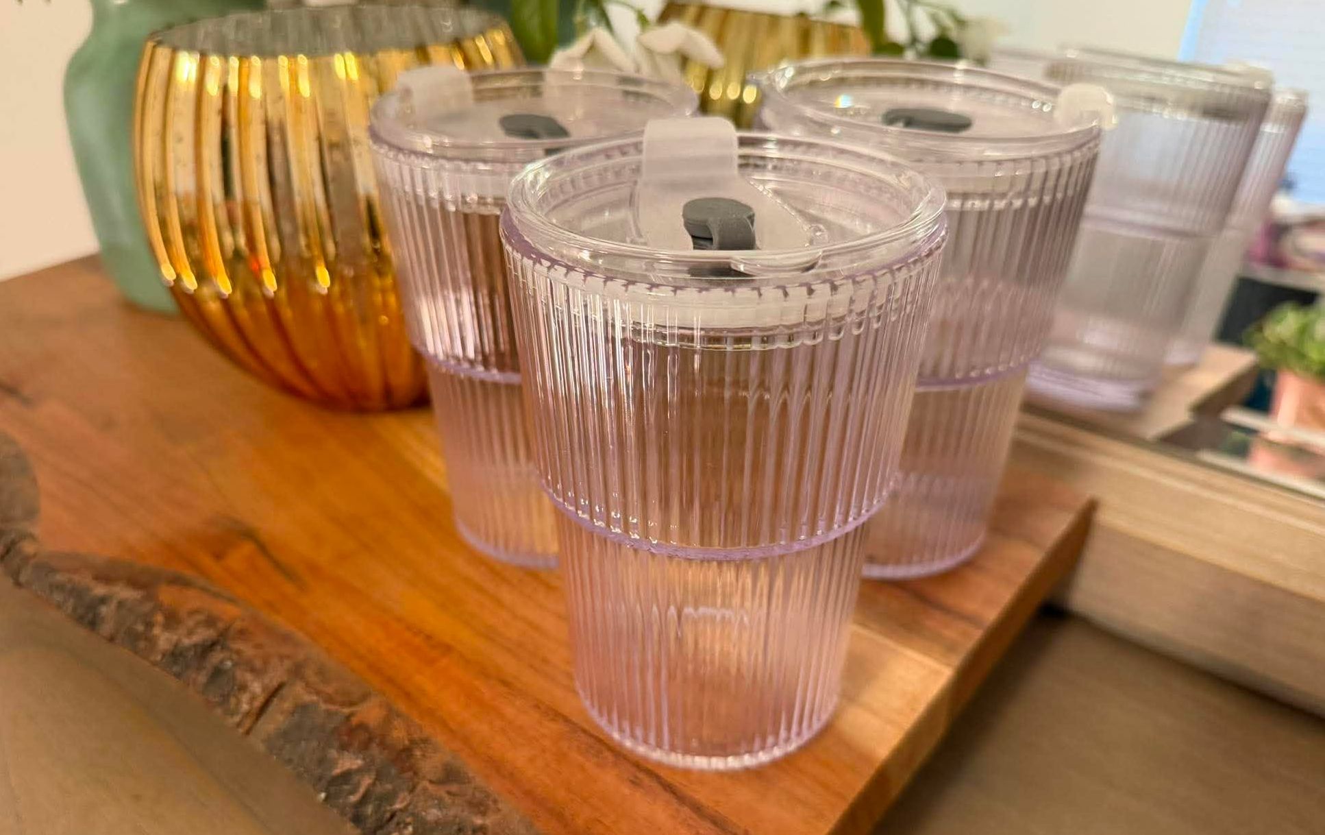 Three clear plastic ribbed tumblers are on a wooden platform.
