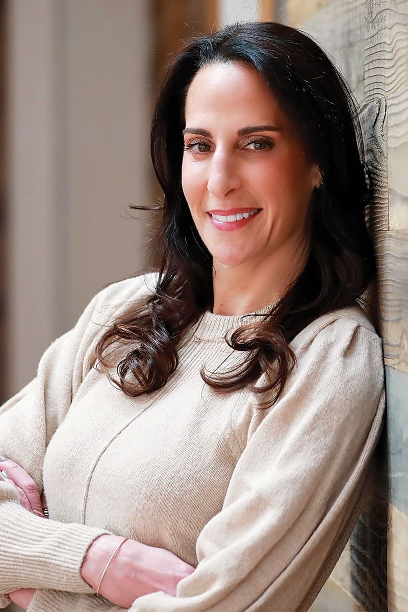 an image of leslie leaning against a wall. she is waring a white sweater