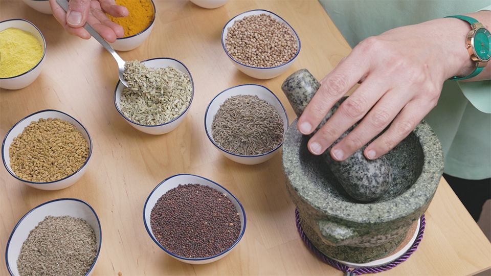Ayurvedische Gewürze in Schalen – Fenchel, Kurkuma, Koriander, Bockshornklee und Senfsamen mit Mörser.