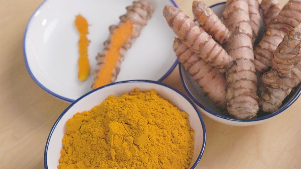 Frische Kurkumawurzeln und leuchtend gelbes Kurkumapulver in weißen Schalen – ayurvedisches Heilgewürz