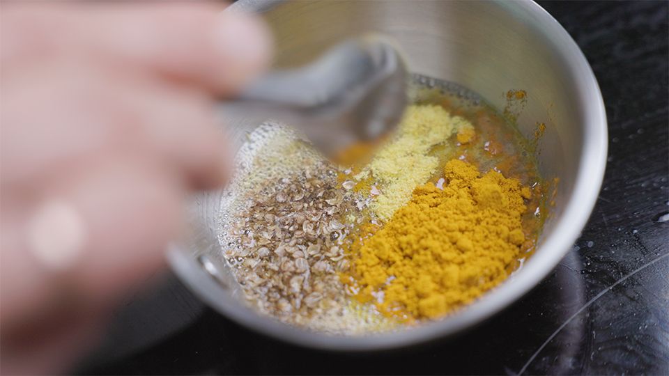Ayurvedische Gewürze – Koriandersamen, Kurkuma, Asafoetida und Ingwerpulver werden in einem Topf mit Ghee angeröstet
