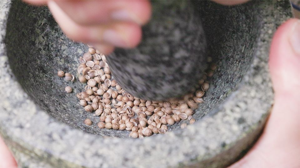 Frische Koriandersamen im Steinmörser – Gewürze selbst mahlen nach Ayurveda