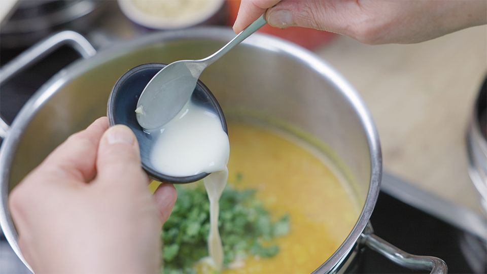 Kokosmilch wird in eine ayurvedische Dal-Tomatensuppe mit Zimt und frischen Kräutern eingerührt