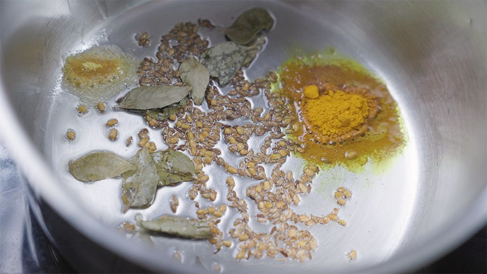 Kreuzkümmel, Lorbeerblätter, Kurkuma, Bockshornklee und Asafoetida werden in Kokosfett angeröstet – ayurvedische Gewürzbasis im Topf
