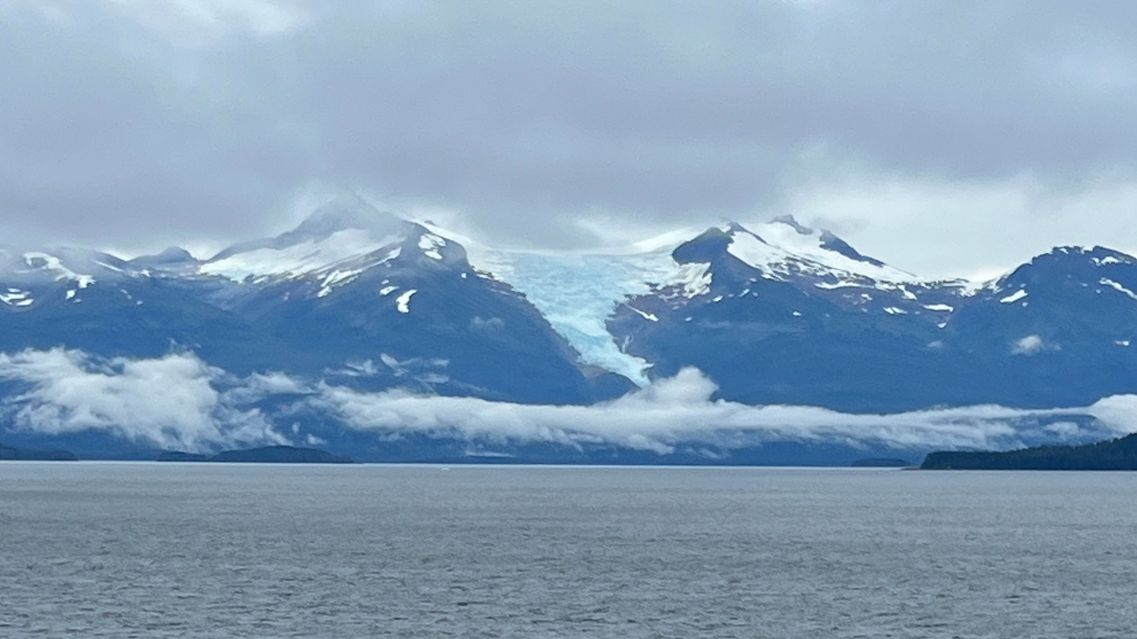 Juneau Cruise Port: Snowcapped glacier mountains and cloudy skies seen from the water.