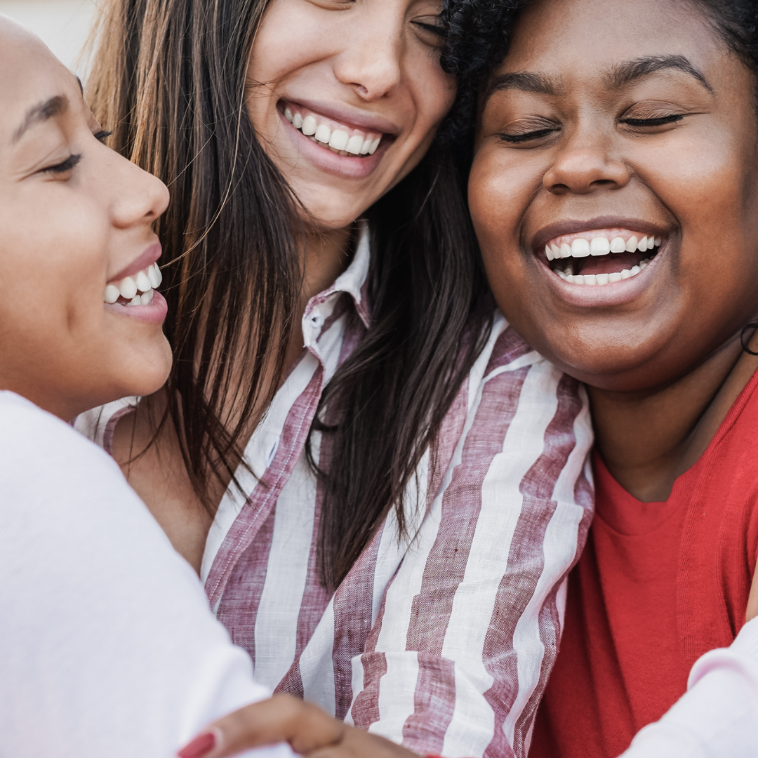Three racially diverse women smiling and hugging.