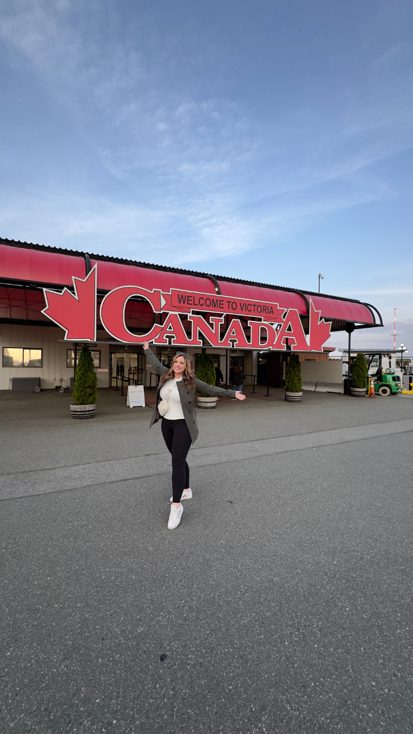 Victoria Cruise Port: Professor Melissa posing in front of large 'Welcome to Canada' sign at the terminal