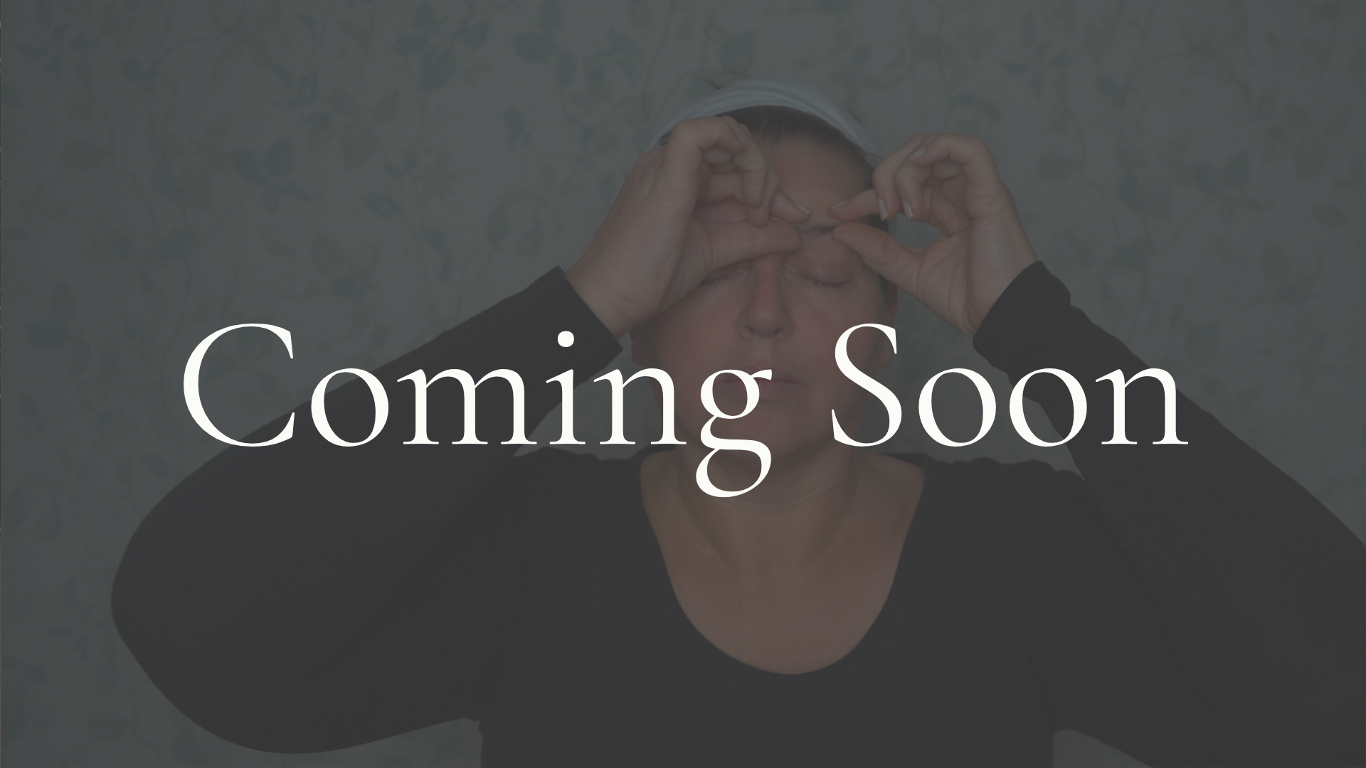 Face yoga teacher practicing a calming face yoga exercise with fingers placed at the corners of the mouth and eyes closed