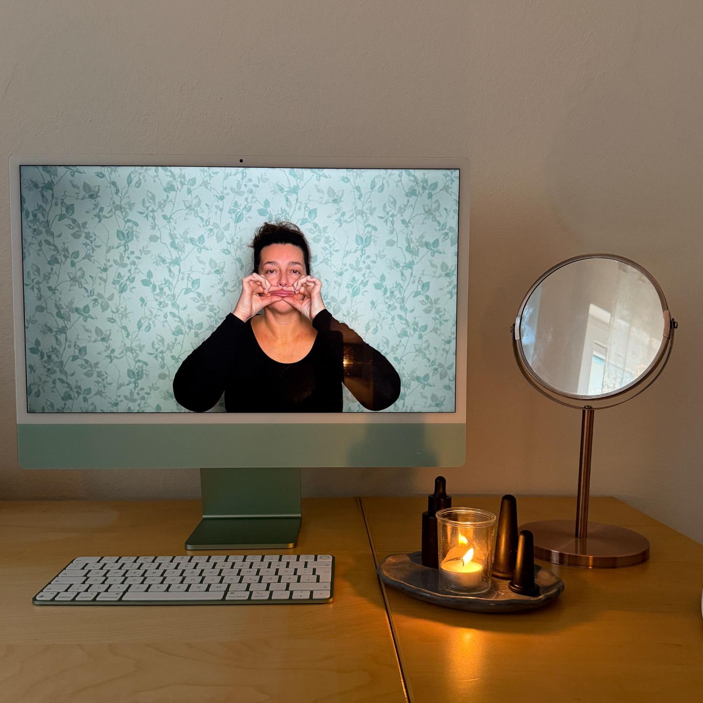 Face yoga teacher demonstrating a face yoga exercise on a computer screen at a desk