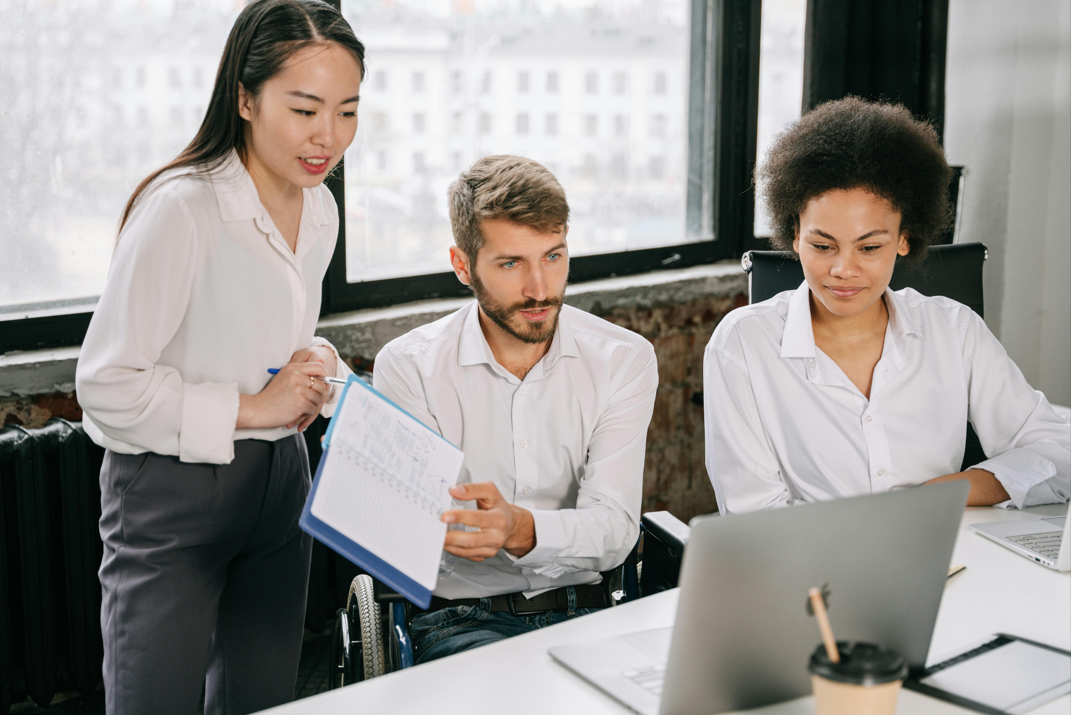 A team of three coworkers engaged in a calm discussion around a laptop during a workplace meeting.