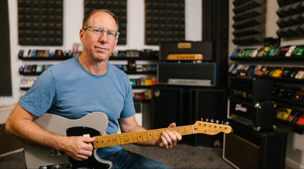 Brian Wampler playing a silver Telecaster guitar in a studio setting filled with pedals and amps