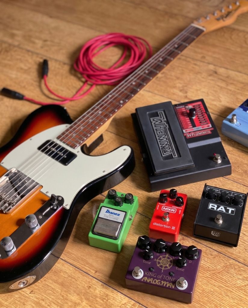 Close-up of a sunburst Telecaster guitar with colorful guitar pedals on wood flooring