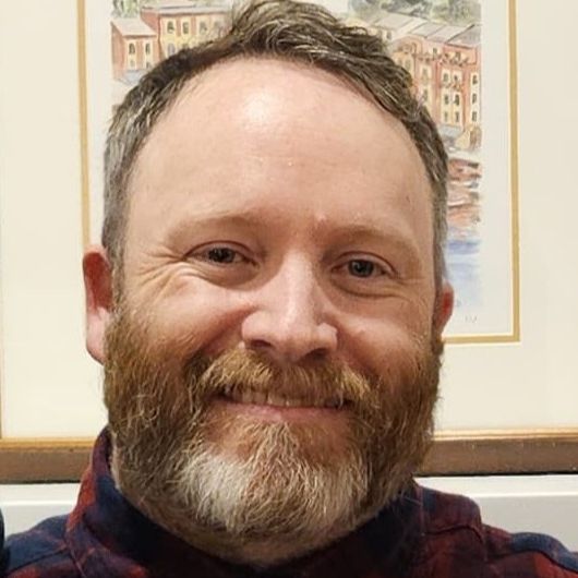 Headshot of Colin McDannel, caucasian man with brown hair and red beardcas