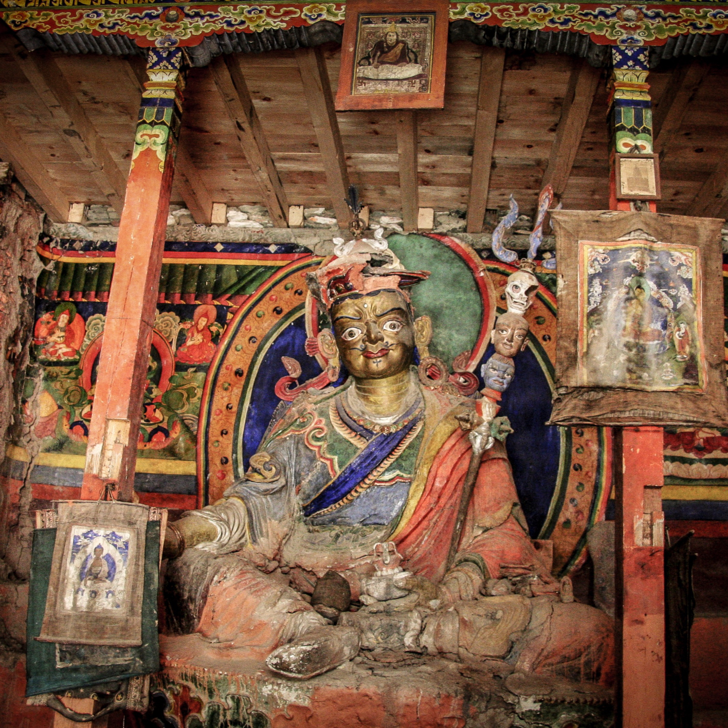 Buddha statue on a Tibetan altar with wrapped scriptures and ritual objects.