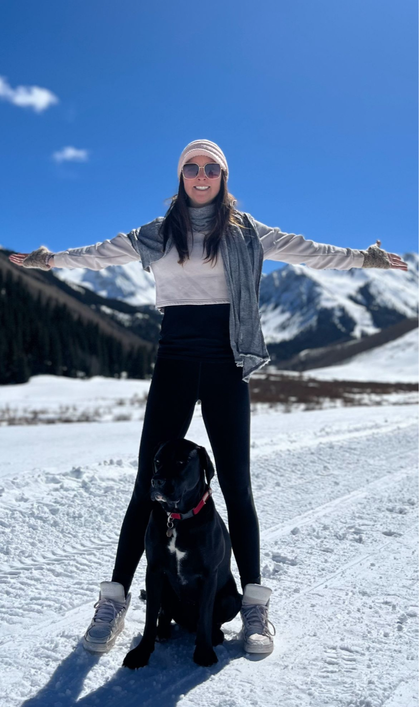 Sara Broome, colon cancer survivor and founder of The Cancer Comeback Club, smiling with her rescue dog Ernesto in the mountains during her cancer recovery journey.