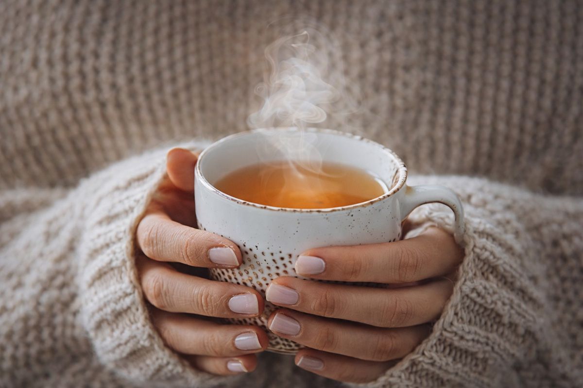 HAnds holding a steaming cup of tea. 