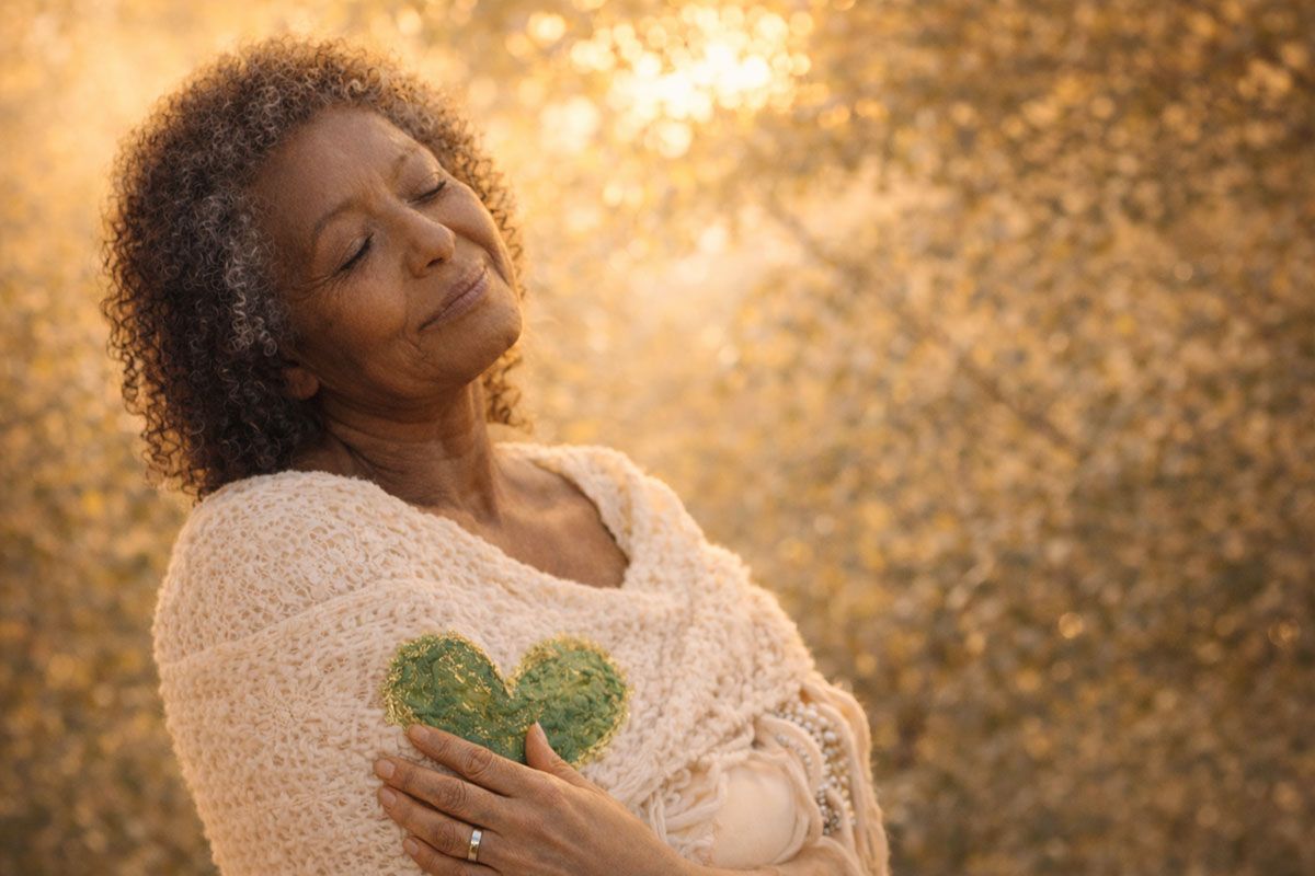 Contented older woman wrapped in a shawl with golden sunlight behind.