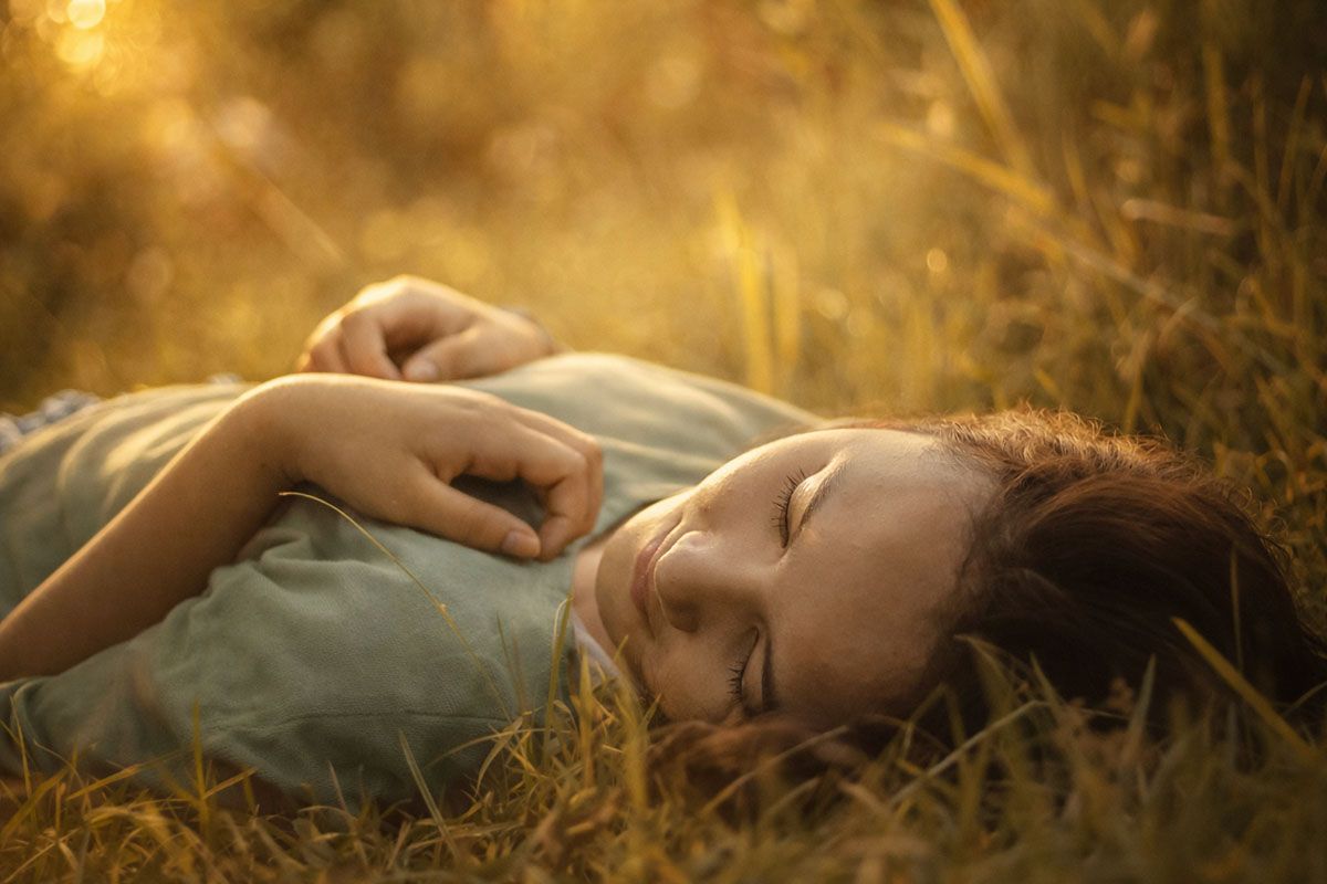 Smilling woman laying in golden grass with eyes closed.d