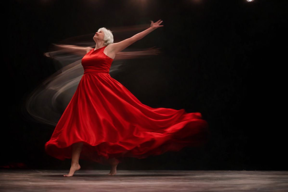 Artistic image showing Debroah dancing with joy in a bright red ball gown. 