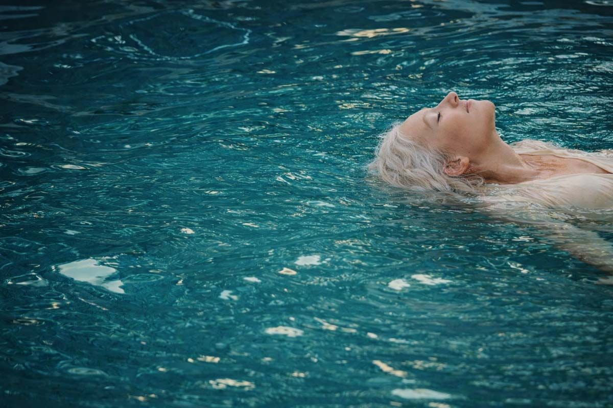Relaxed woman with closed eyes floating in an aqua pool.