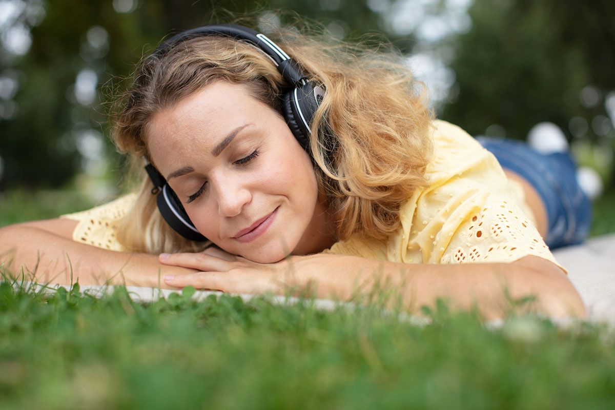 Contented woman laying on grass wearing headphones.