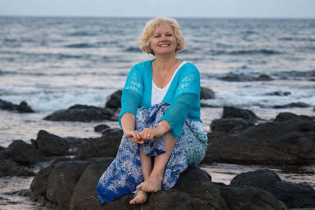 Smiling Deborah Christensen sitting on a rocks by the ocean.