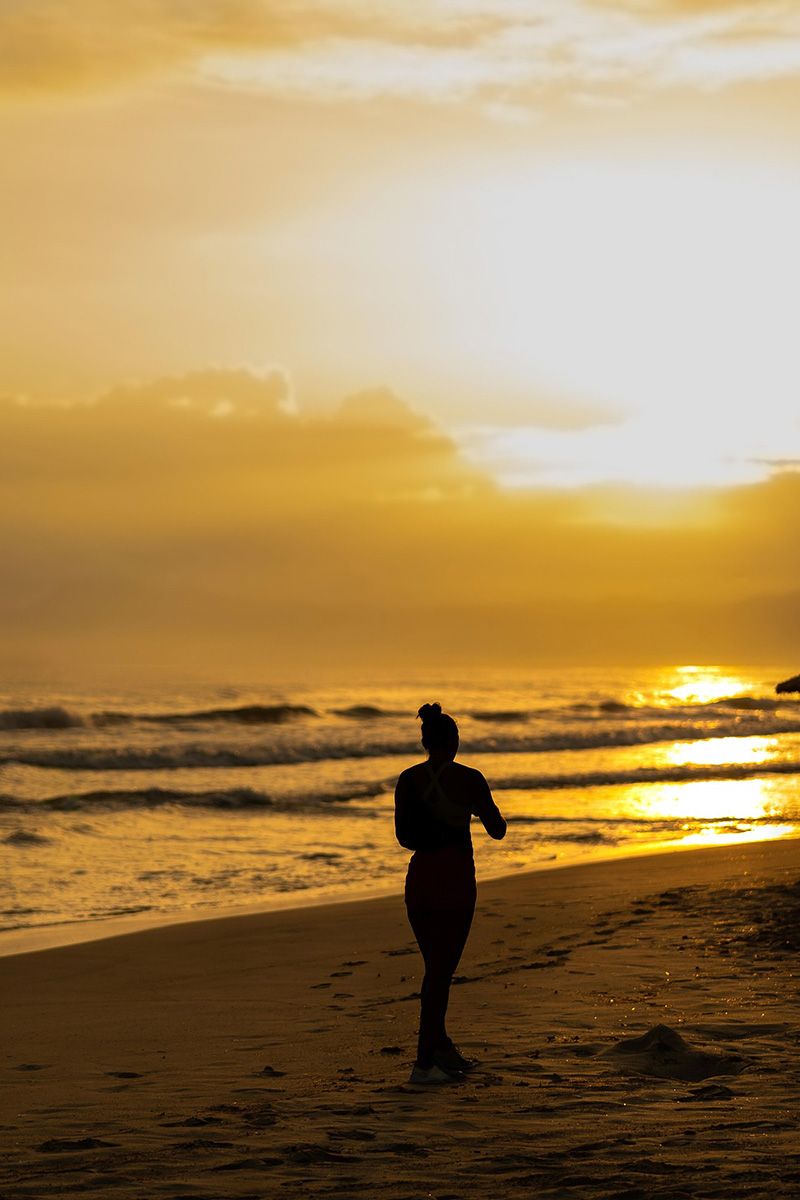 Silhouette of woman walking on golden sunrise beach. 