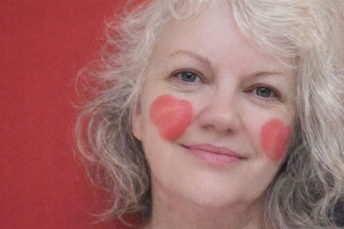 Close up portrait of Deborah with red hearts painted on her cheeks.  