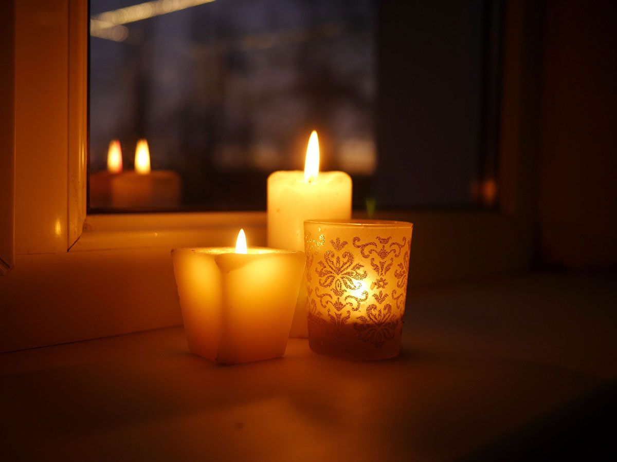 Three candles on a window sill give off a warm glow.
