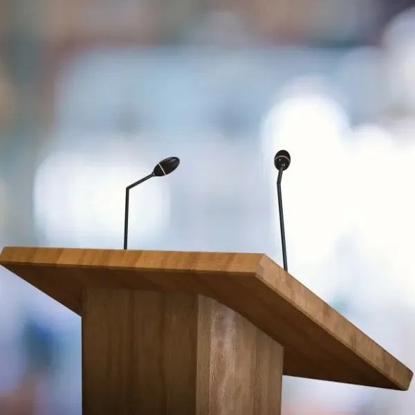 brown speaker podium with two microphones on a blurred light colored background