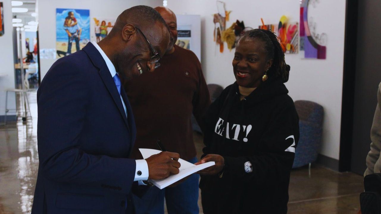 Dr. Michael Thompson smiling as he receives a book to sign from someone.