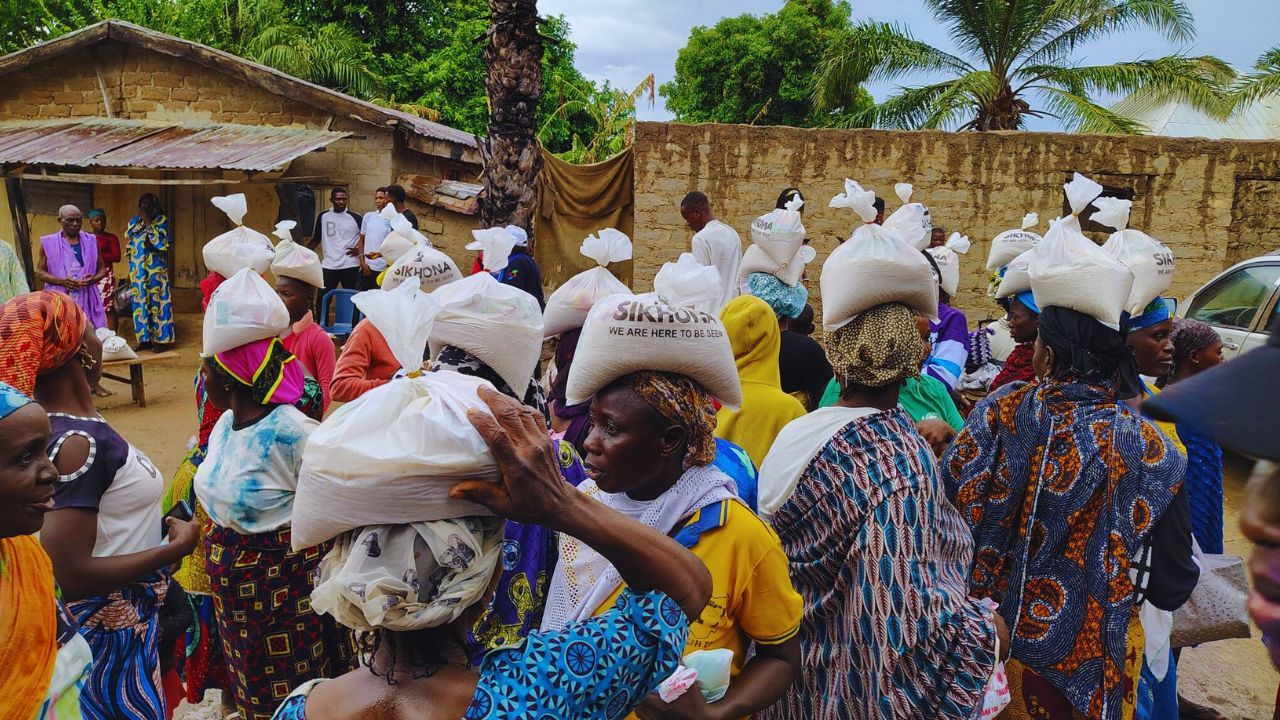 People carrying plastics of rice on their heads while walking in a line.