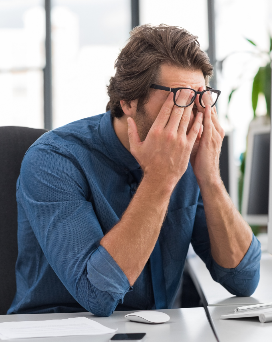 Overwhelmed business man at desk with hands over face looking