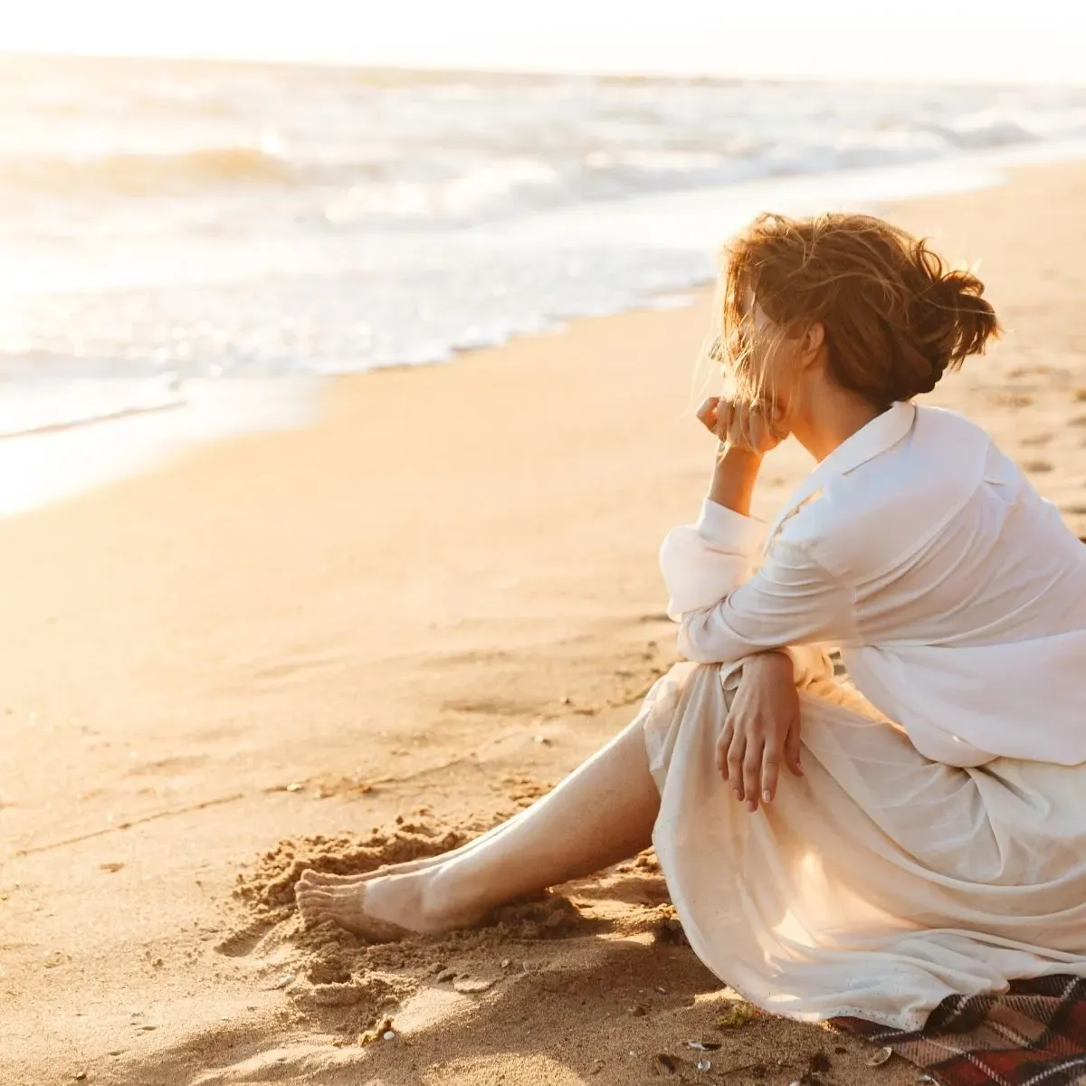 midlife woman in white blouse and skirt looking out at ocean