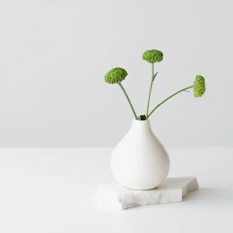green stems in white vase on block of marble on white surface with white background