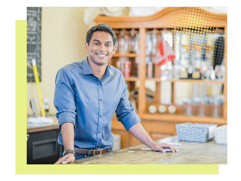 interior of workroom, smiling man looks at the camera, hands resting on the bench in front of him