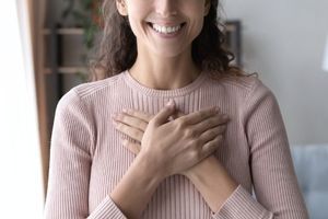 woman smiling while putting her hands on top of her heart