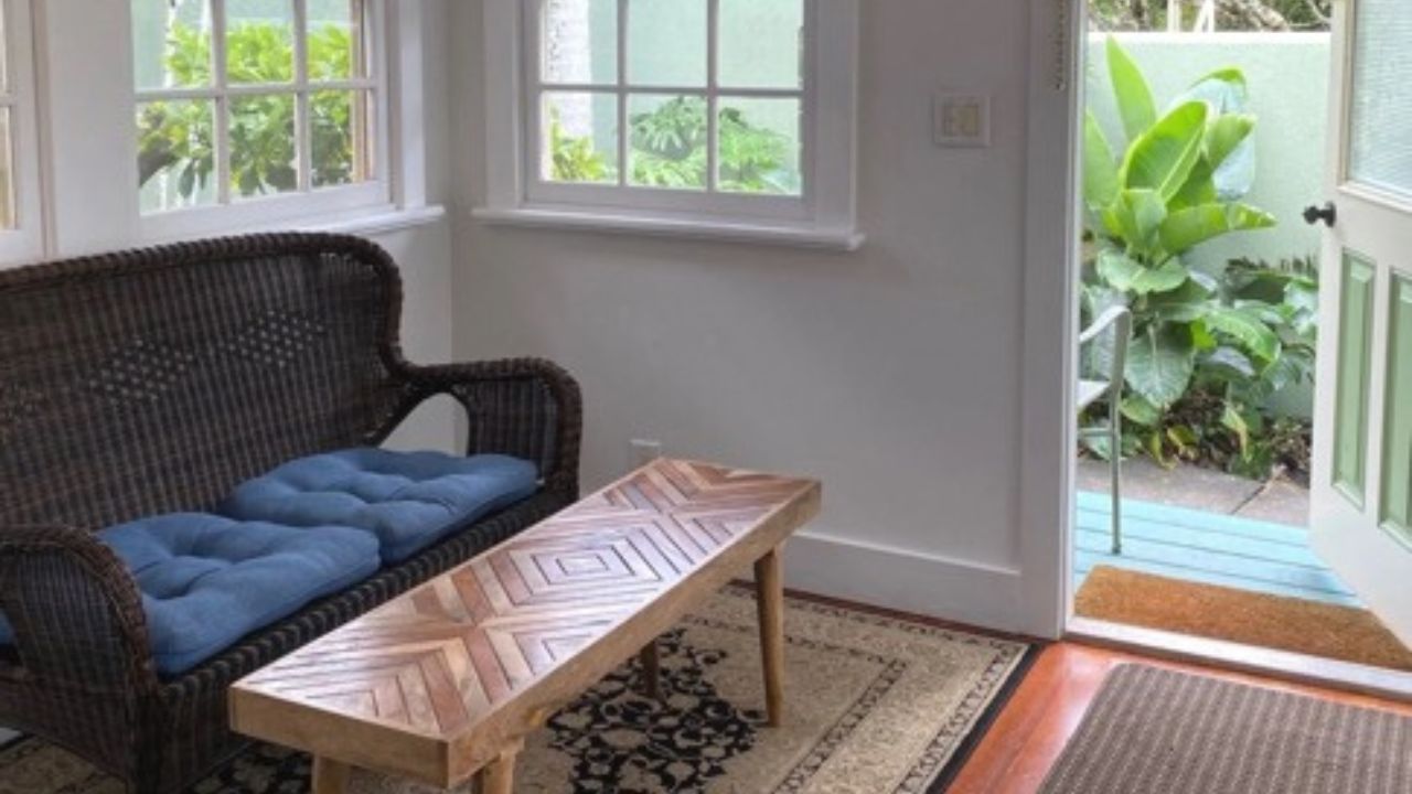 A cozy sitting area with a wicker sofa and geometrically patterned table overlooks a lush garden through an open doorway.Accommodations Hawaii Full Body Energy Orgasm Retreat 