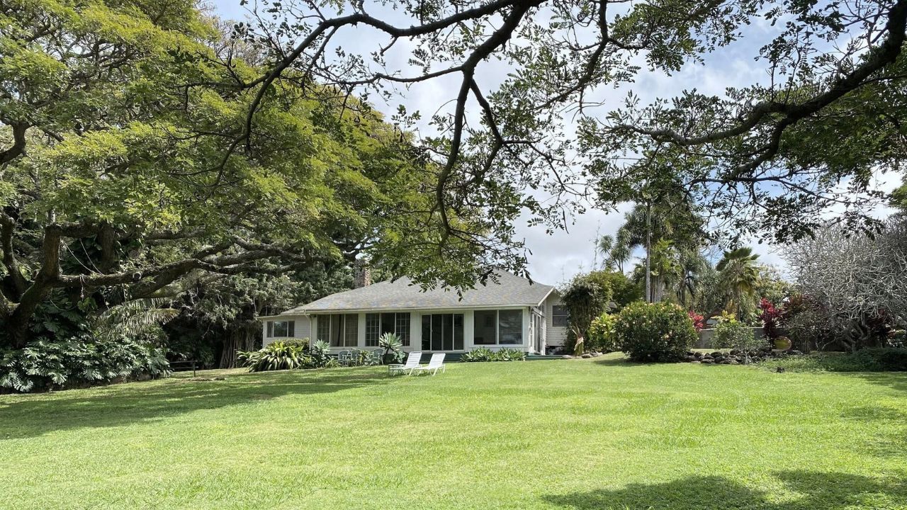 A white house with a sunroom sits on a large lawn with mature trees. Hawaii Full Body Energy Orgasm Retreat 