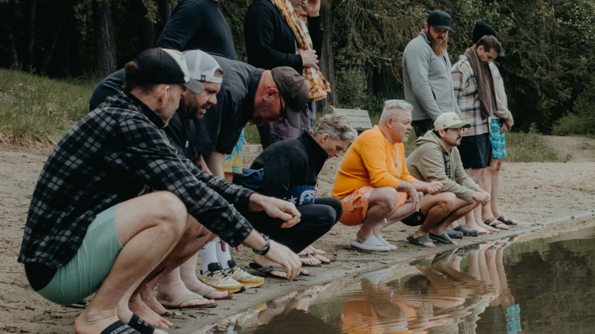 Men crouching together at the edge of a lake