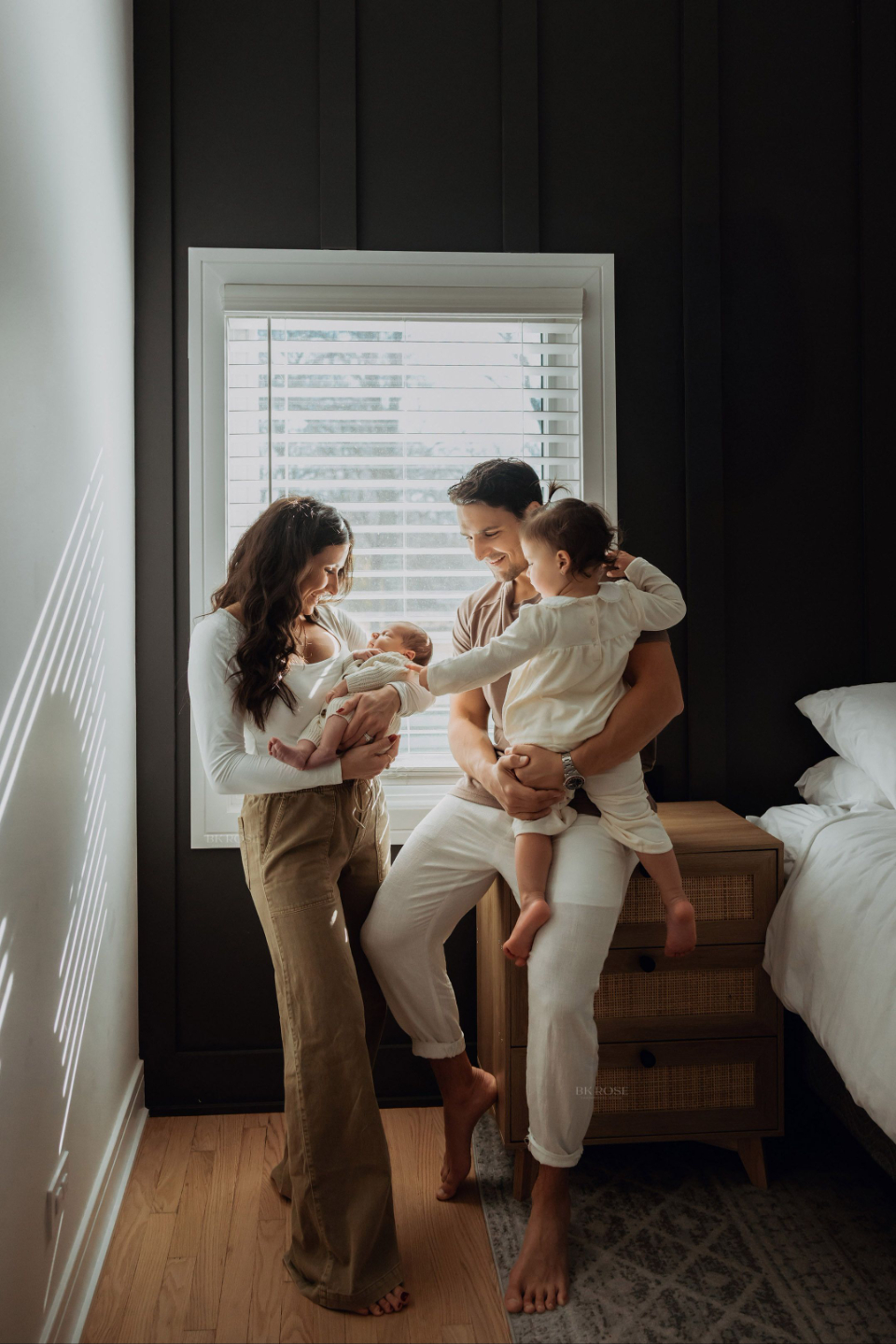 family of four lovingly looking down at newborn baby