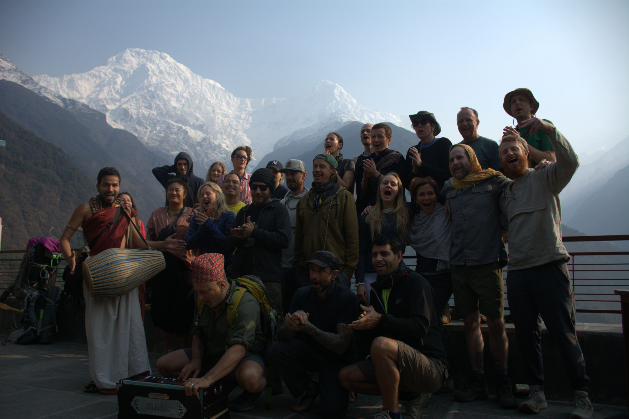Group of spiritual pilgrims chanting and singing kirtan in the Himalayas during a yoga and bhakti pilgrimage in India, with snow-capped mountains in the background