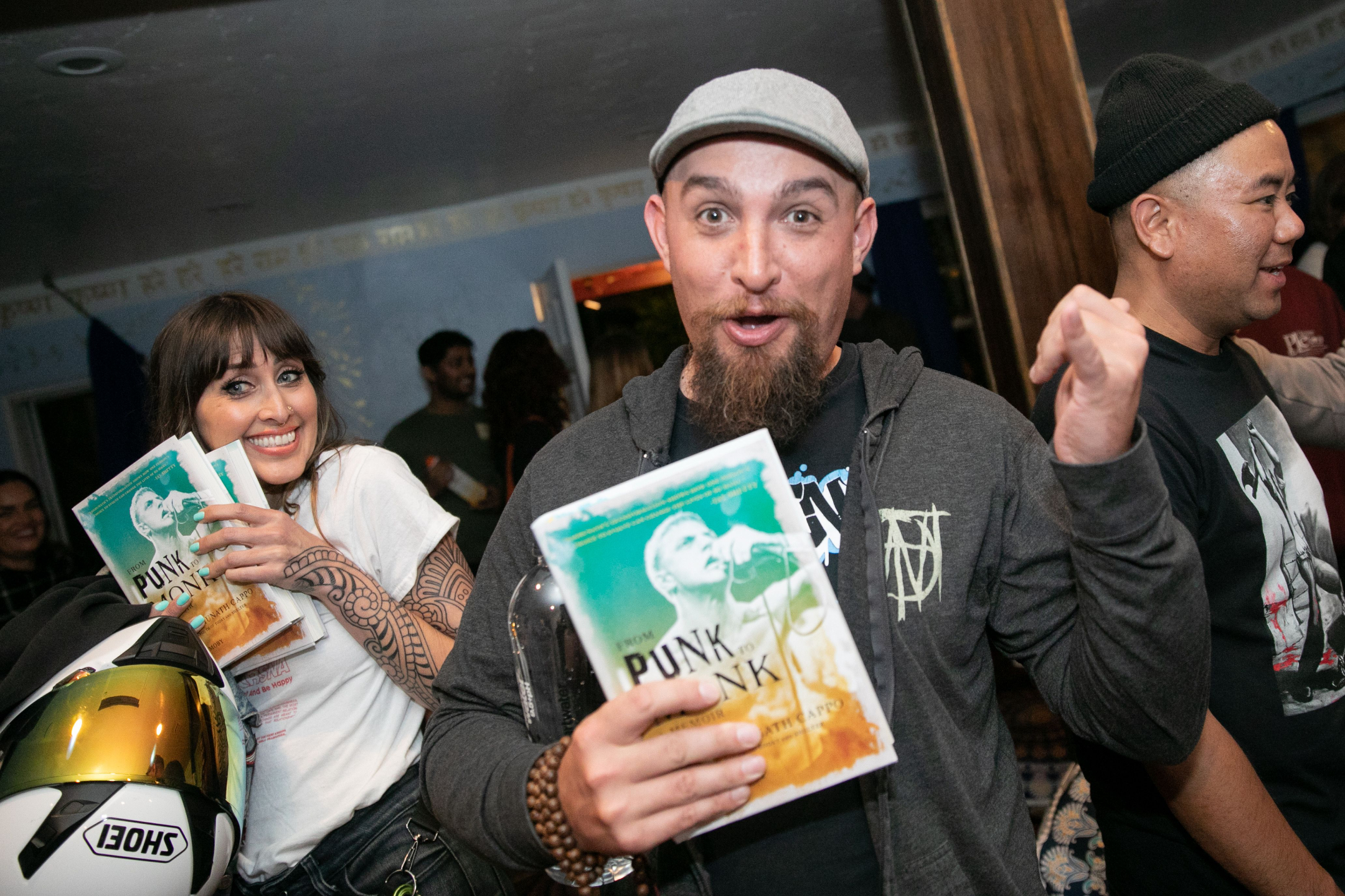 People at a lively book event holding copies of From Punk to Monk, smiling and celebrating, with the book cover clearly visible in the foreground.