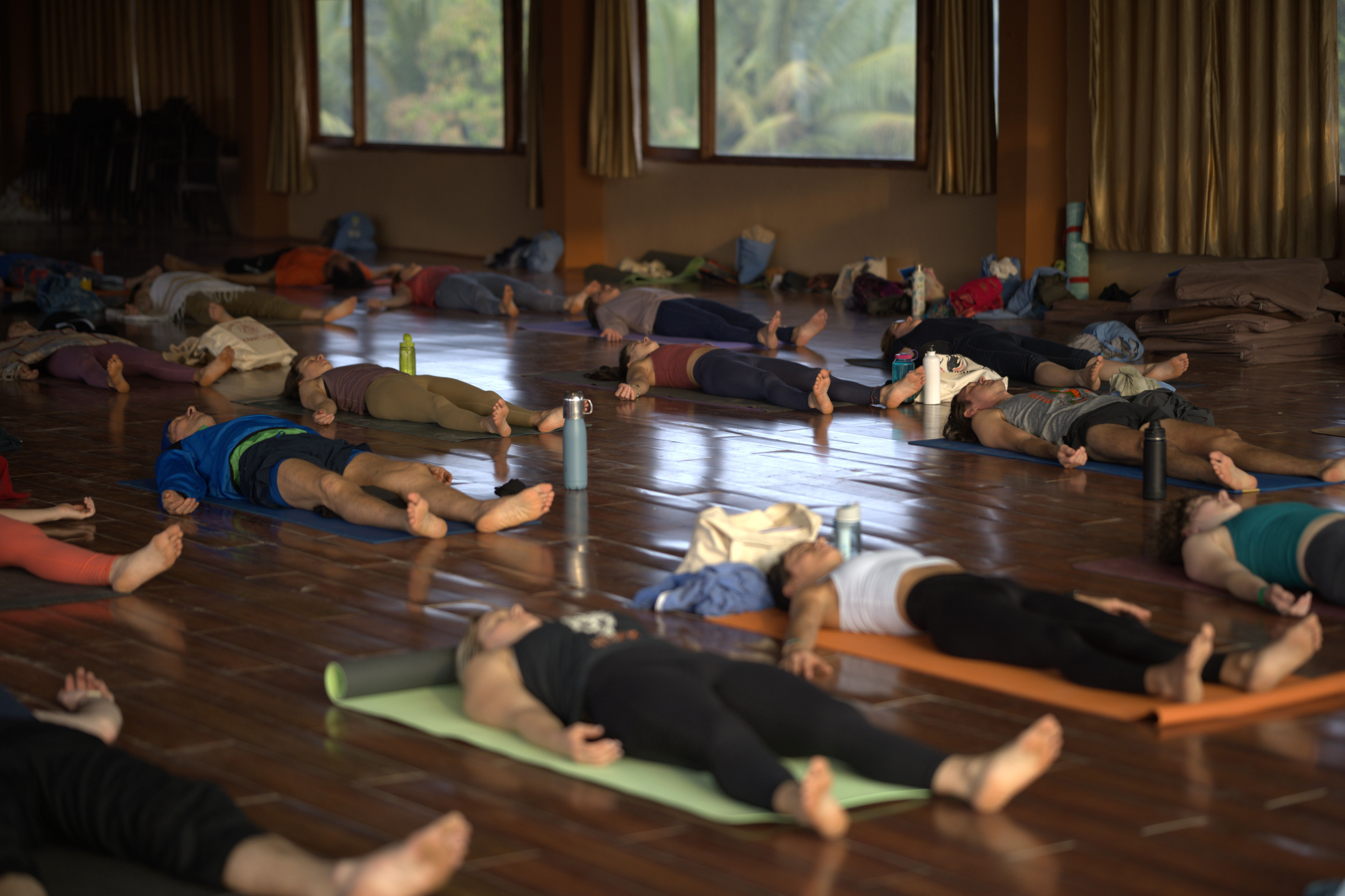 Group yoga class resting in savasana during a yoga teacher training in India, with students lying on mats in a peaceful retreat space